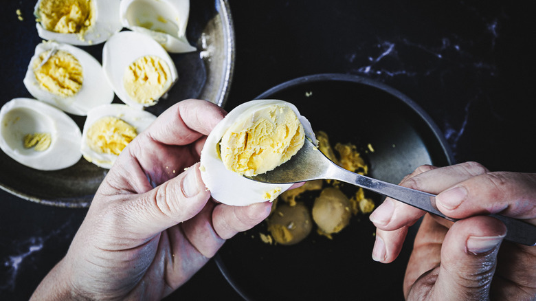 hand removing yolk from boiled egg half