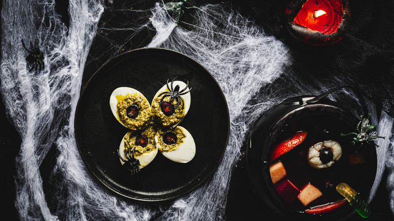 four deviled eggs with plastic spiders on black plate with cauldron