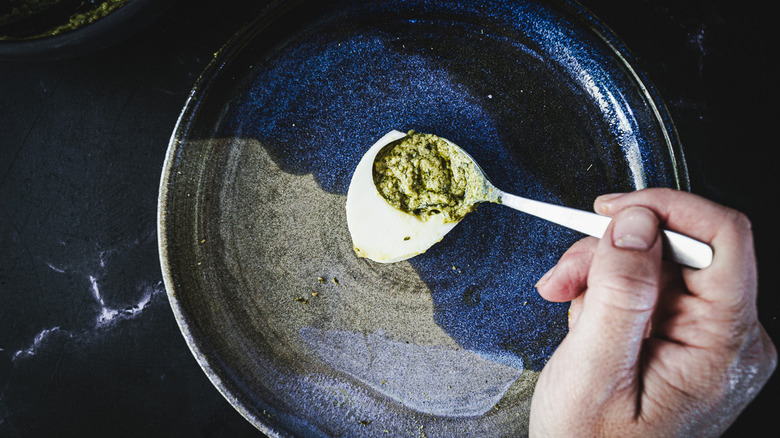 hand adding pesto filling to deviled egg half