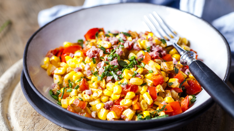 canned corn in a salad with chopped tomatoes, herbs, and ham in a bowl