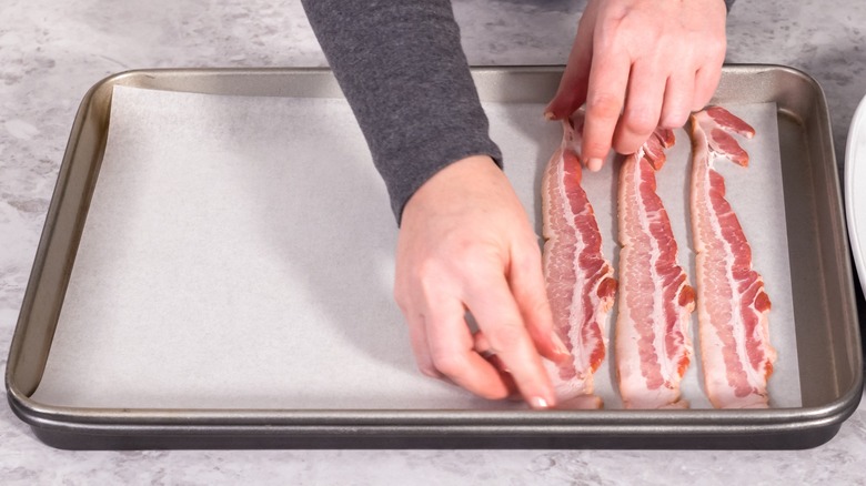 Placing raw bacon strips on a baking sheet