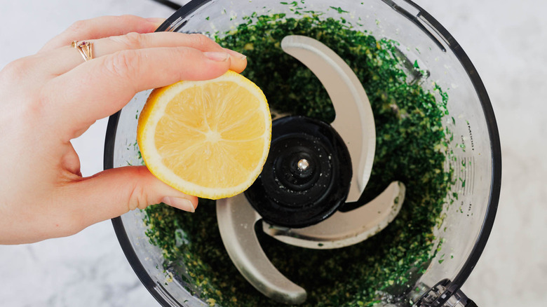 Adding lemon to pesto in food processor bowl