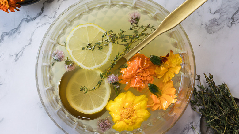 A bowl with lemon slices, herbs, flowers and a yellow drink with a ladle