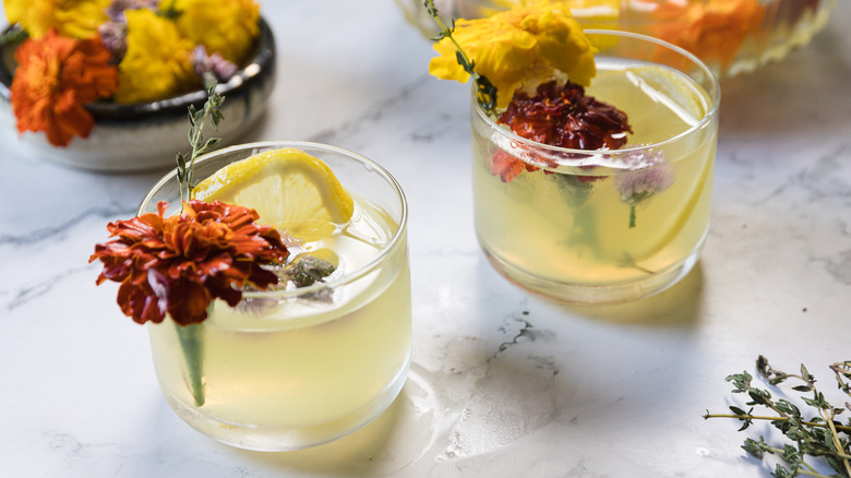 Two glasses with a yellow liquid, flowers and thyme and lemon slices