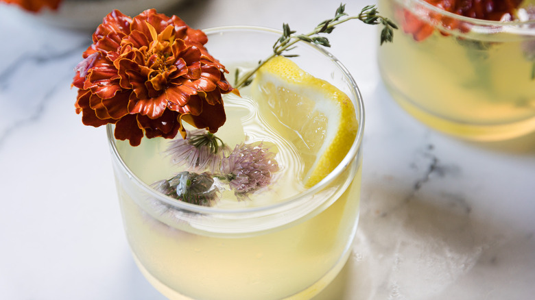 A glass with yellow drink and edible flowers and thyme