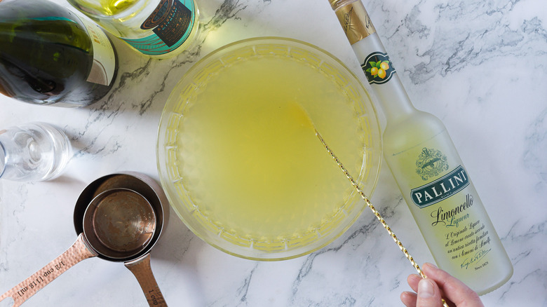 Hand stirring a large bowl of punch with other ingredients around