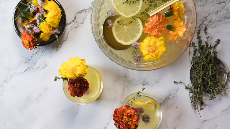 Large bowl of punch with a ladle alongside two glasses with flowers and herbs