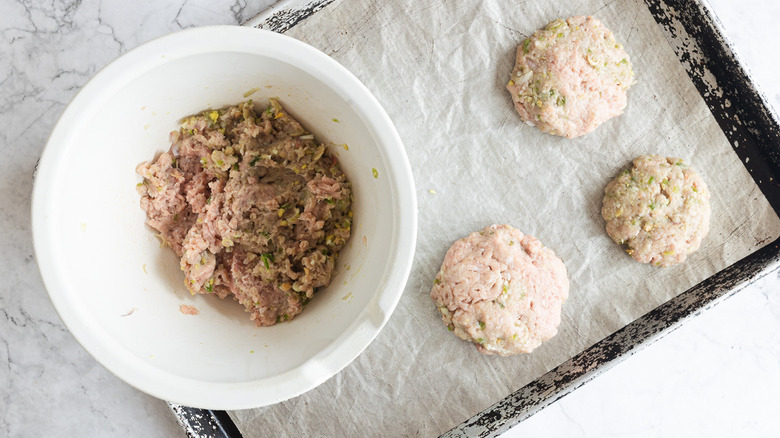 Ground burger mix in bowl beside 3 patties on baking sheet