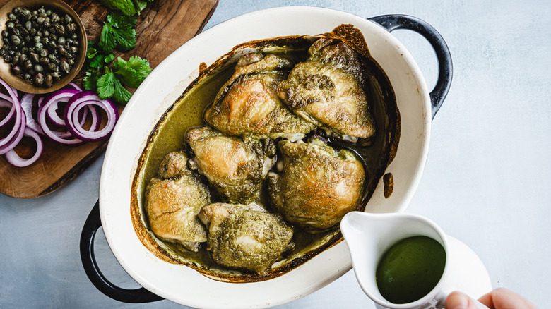 Pouring green herb sauce on baked chicken