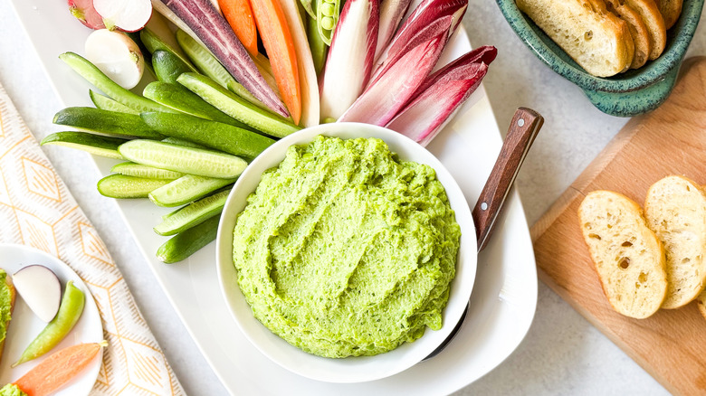 Herby spring pea dip in serving bowl with crudites and baguette slices