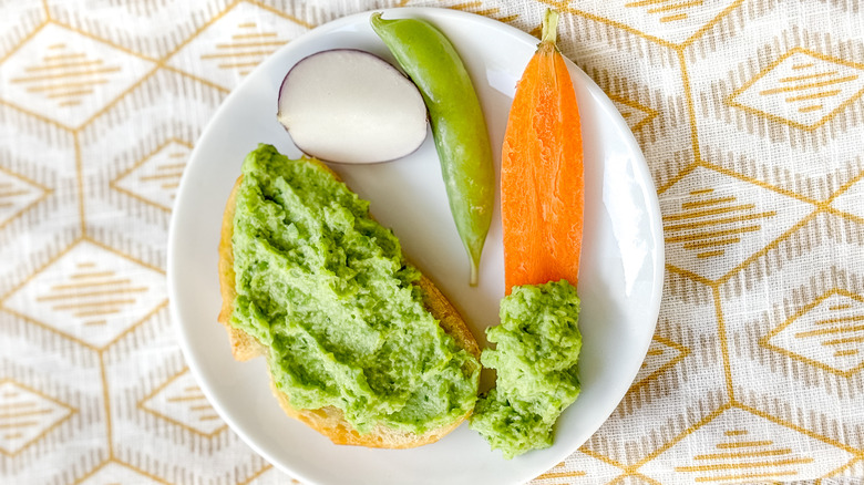 Herby spring pea dip on baguette slice with crudites on plate