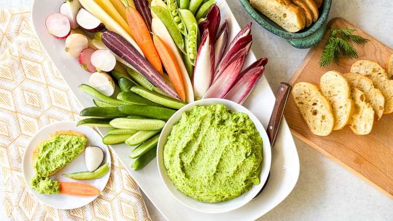 Herby spring pea dip with crudites and baquette slices on serving platters
