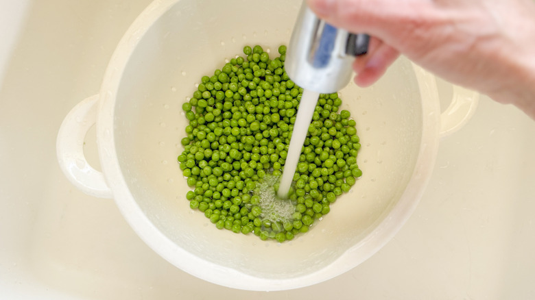 Rinsing cooked fresh peas in colander in sink