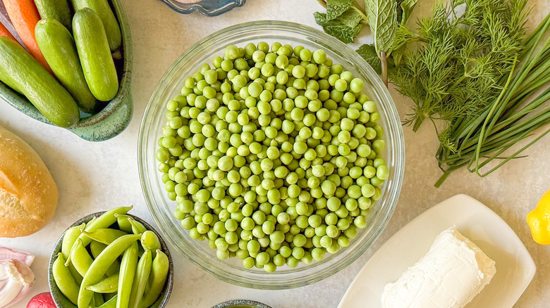 Bowl of English peas surrounded by vegetables, herbs, and goat cheese 