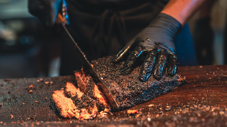 Someone with black gloves slicing a brisket