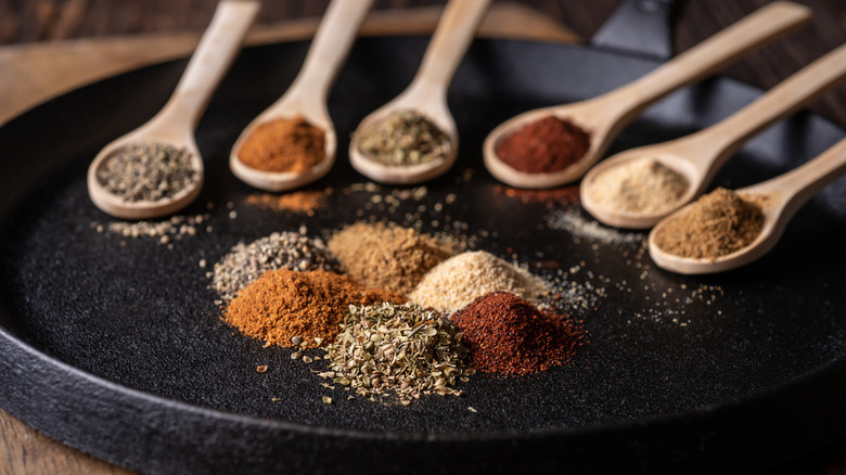 Various spices on a black dish and on wooden spoons