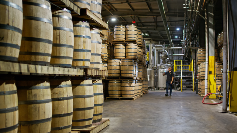 distillery worker walking through a warehouse checking oak barrels