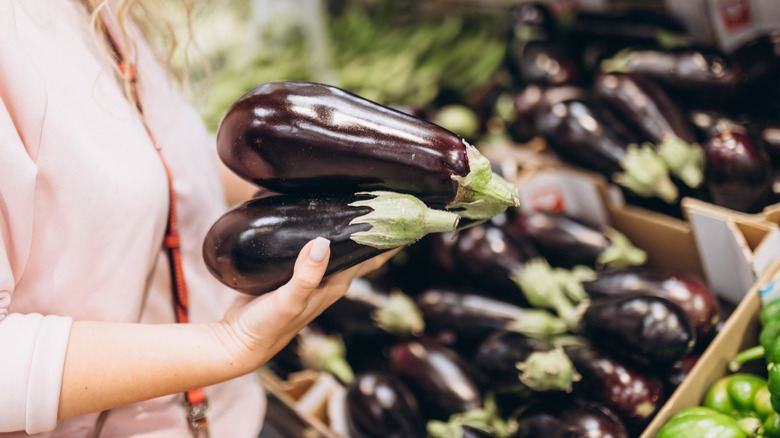 woman selecting eggplants at grocery store