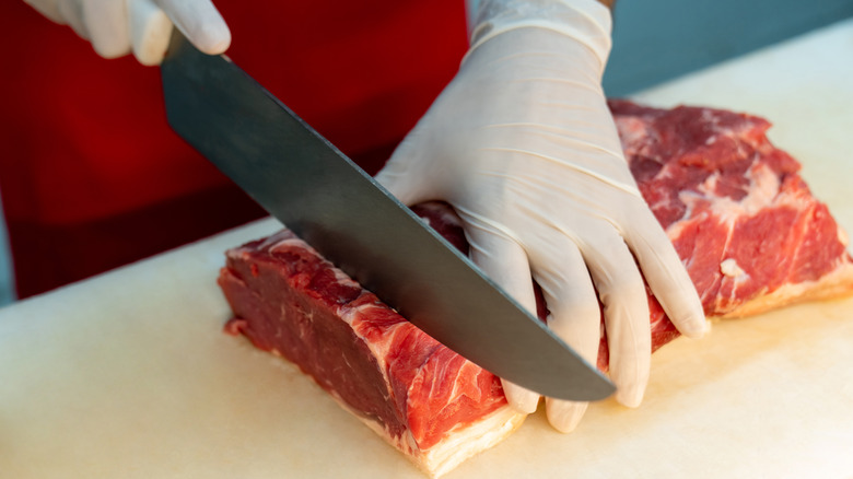 Hands cutting raw meat