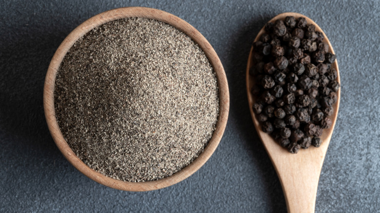 bowl of ground black pepper and spoon of peppercorns