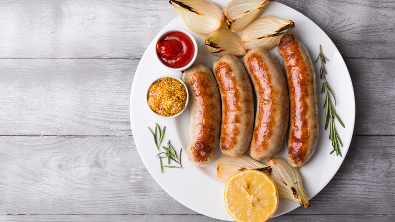 Four cooked sausages next to ketchup, mustard, onion, and lemon half on plate