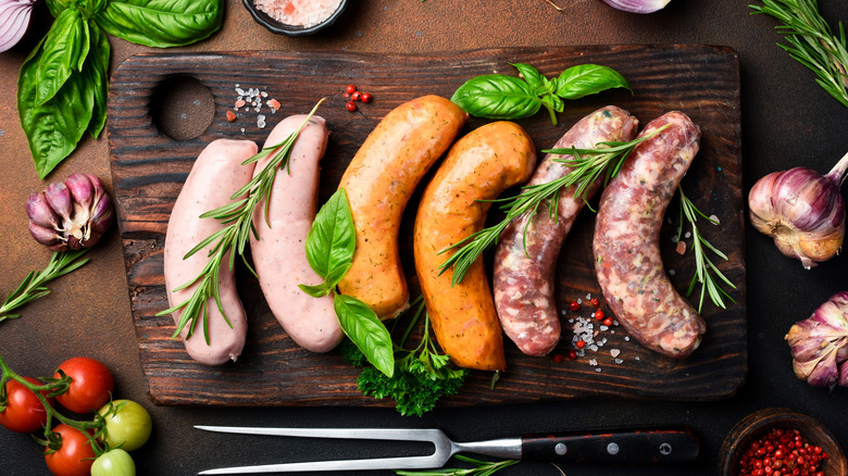 Variety of 6 sausages with basil and rosemary on wooden cutting board