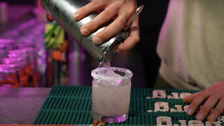 A bartender pouring a margarita into a rimmed glass