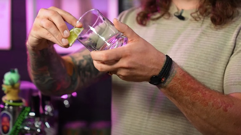 A bartender using a lime wedge to rim a glass