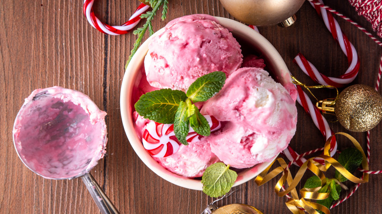 Peppermint ice cream in a bowl, garnished with fresh mint and hard candy, surrounded by candy canes and ornaments