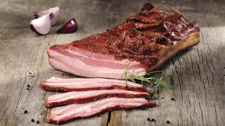 thick-cut slices of bacon lying in front of a full bacon slab on a wood table