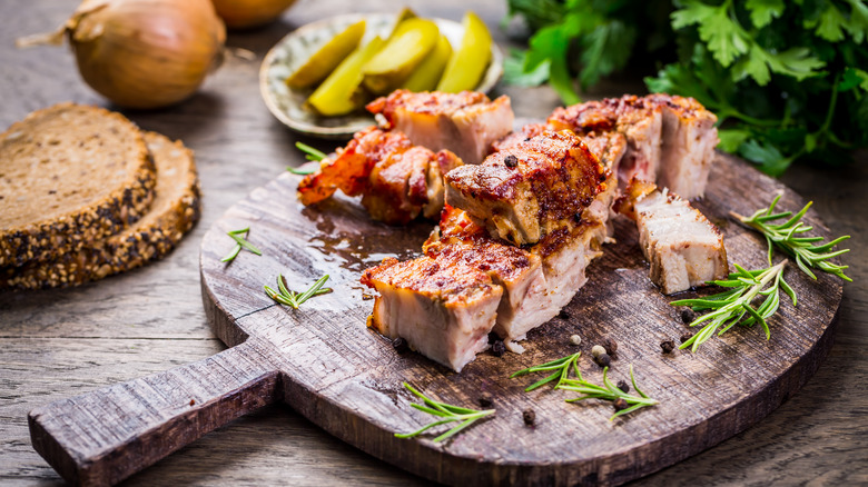 roasted pork belly sitting on a cutting board with sprigs of rosemary