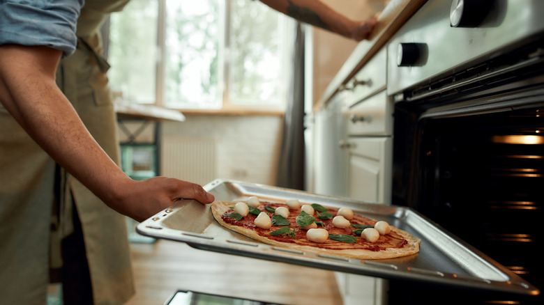 A man places a tray of pizza in an oven