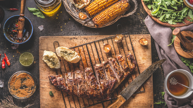 Grilled beef and bread on cutting board with grilled corn and various glazes and rubs