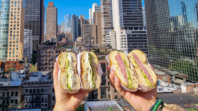 Two people holding bagels against New York skyline