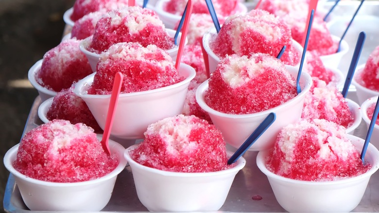 Close-up of several styrofoam cups of shaved ice with red syrup and spoons