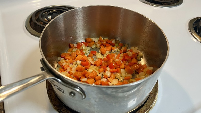a pot with onions, carrots, and red bell peppers