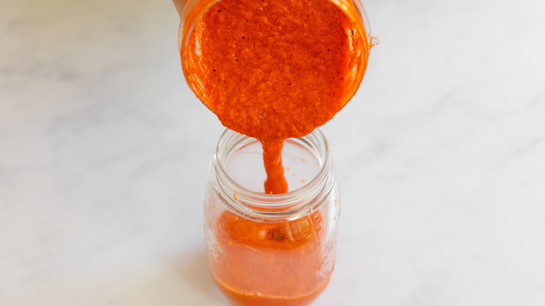 sriracha pouring from blender to jar