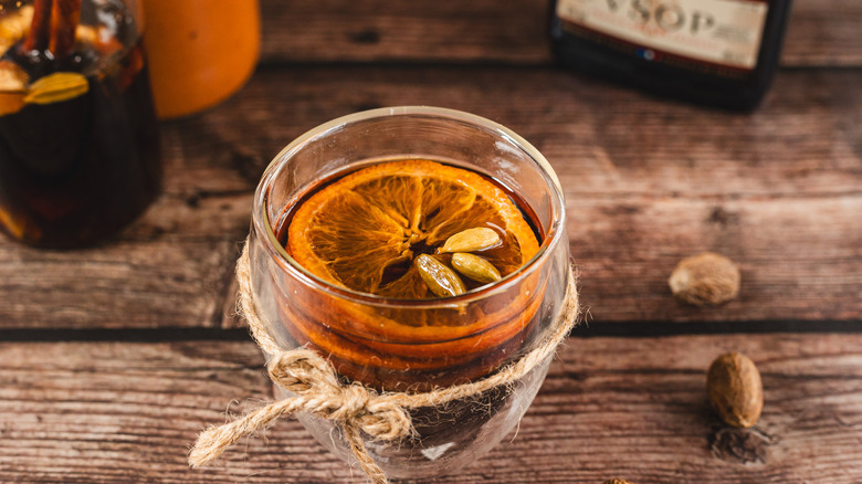 Brown drink with orange slice and cardamom tied with jute string