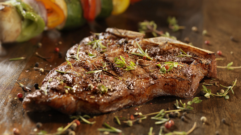 A porterhouse steak rests with fresh herbs around it