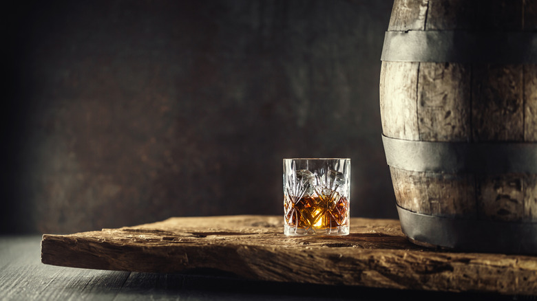 Glass of bourbon on wood next to barrel