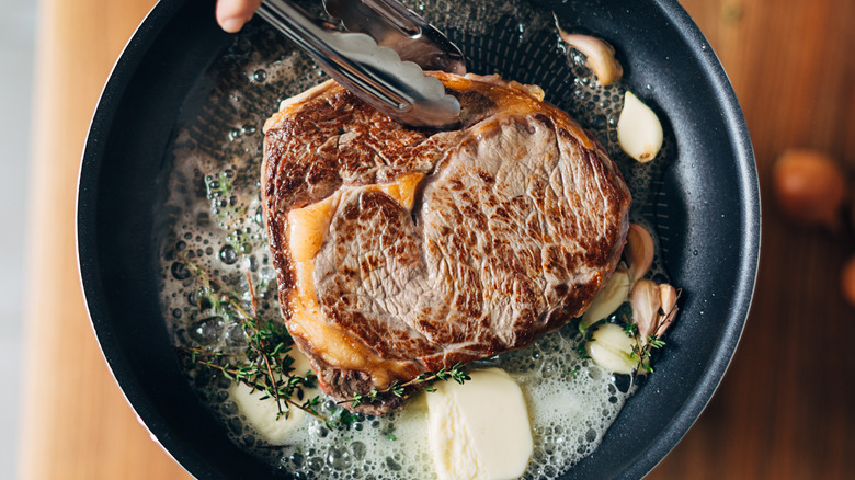 Searing steak in skillet with butter and garlic