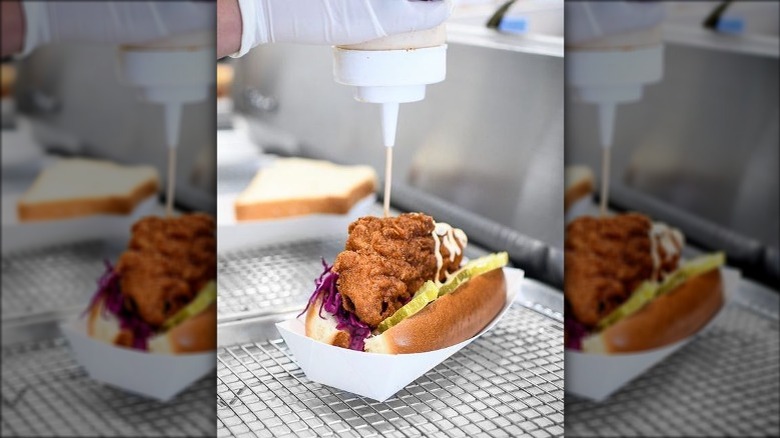 pouring sauce on hot chicken sandwich