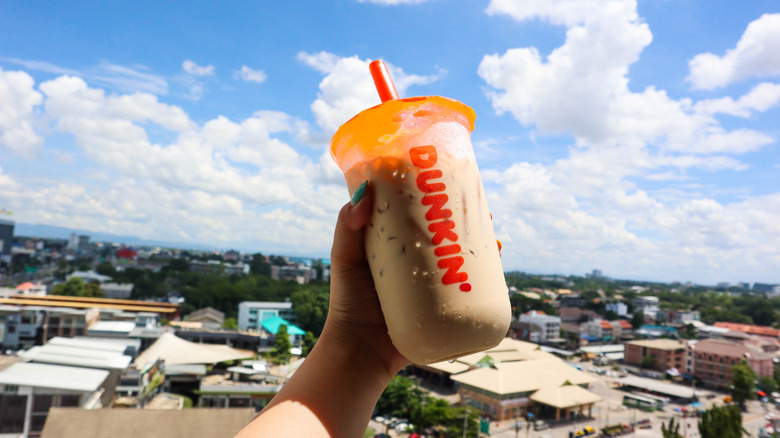 A Dunkin' iced drink against a cloudy sky