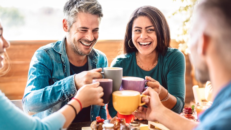 man and woman laughing toasting with mugs