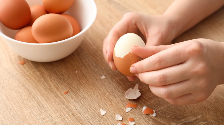 Home cook peeling a hard-boiled egg against a wooden surface