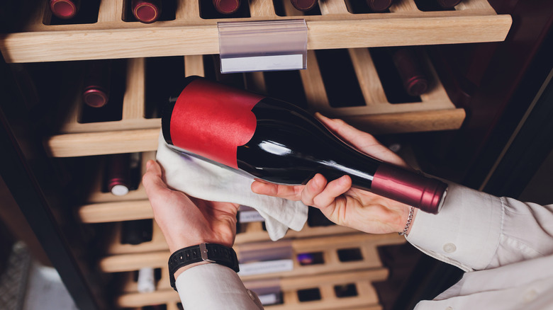 Hand holds wine bottle next to storage 