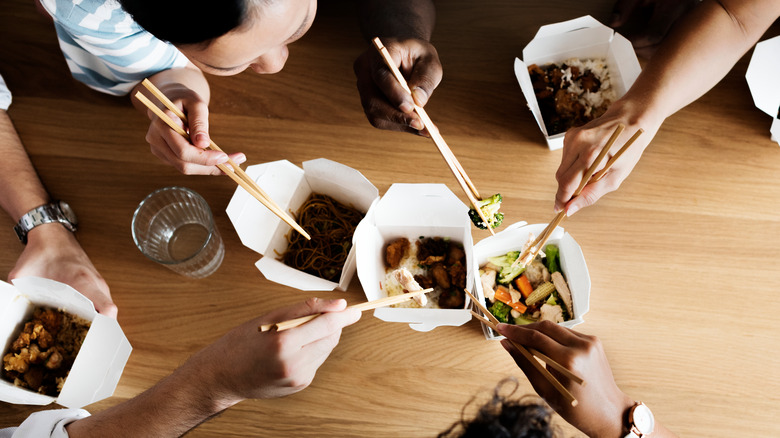 A group of people eats Chinese food with chopsticks