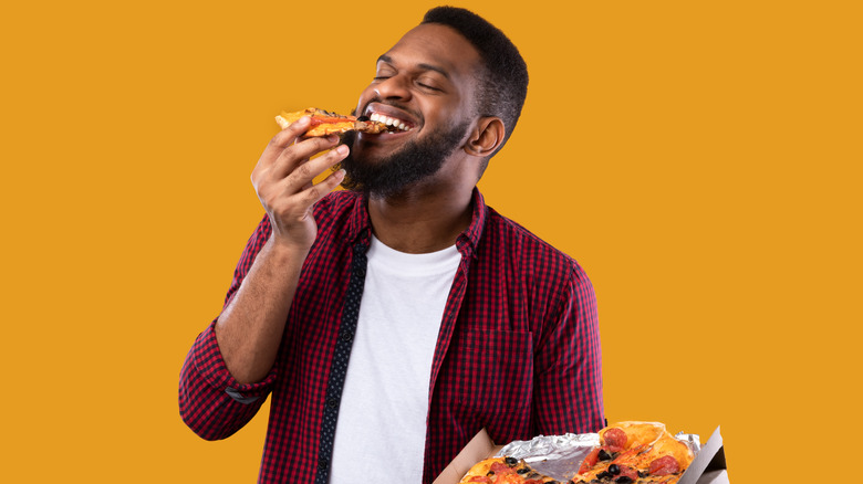 man eating a slice of pizza and holding a pizza box