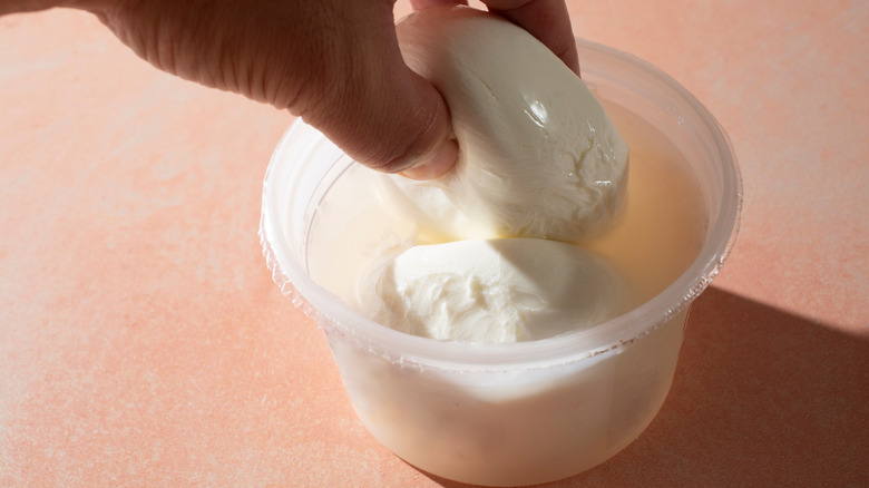 two balls of burrata in a deli container filled with liquid