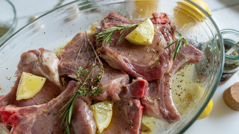 Pork chops in a bowl of brine with lemon and herbs